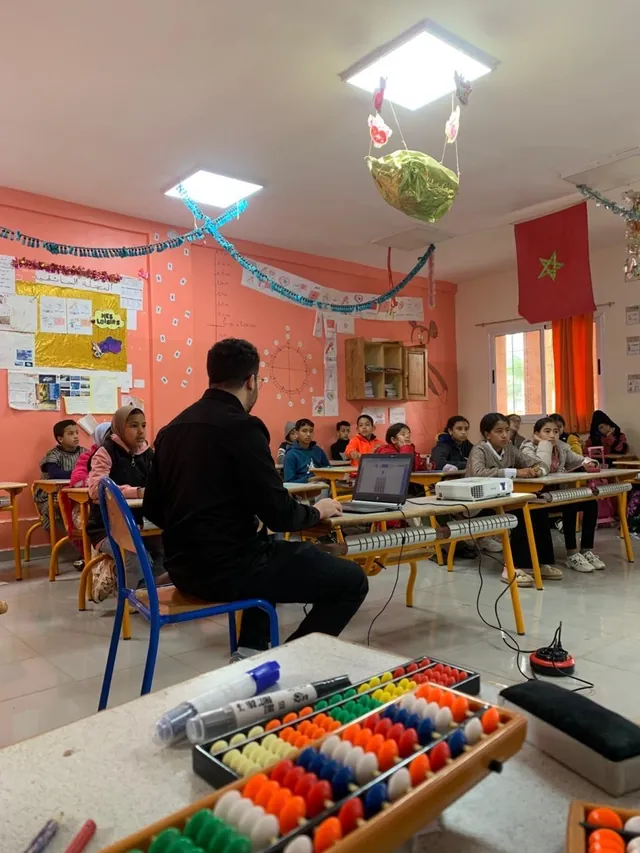 A teacher and pupils in class, with a colorful abacus in the foreground